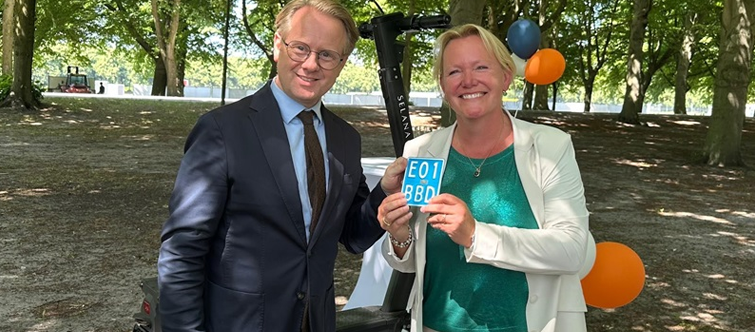 Afbeelding van de minister van Infrastructuur en Waterstaat, Robert Tieman, die op 1 juli 2025 uit handen van Jantina Woudstra, directeur RDW, het eerste kenteken voor een e-step met nationale typegoedkeuring heeft ontvangen.