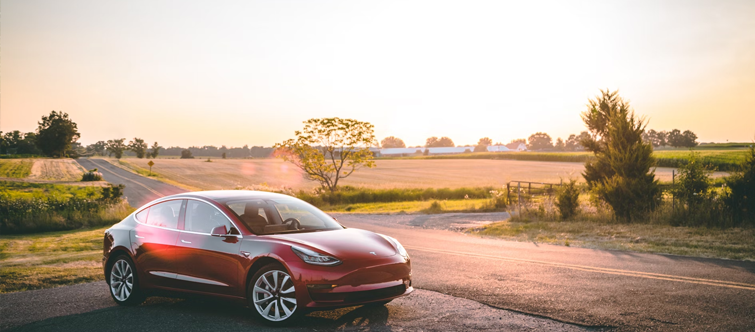 Afbeelding van een Tesla met een ondergaande zon op de achtergrond.