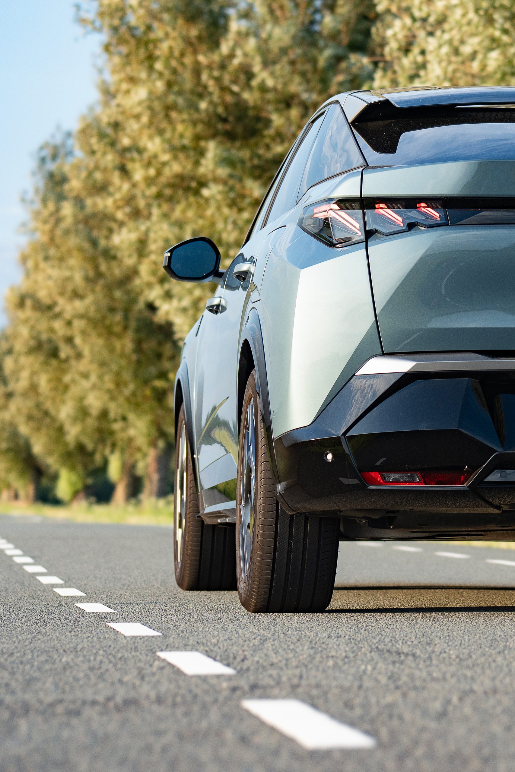 Afbeelding van de auto waarvan de achterkant zichtbaar is. De auto rijdt op een weg langs bomen