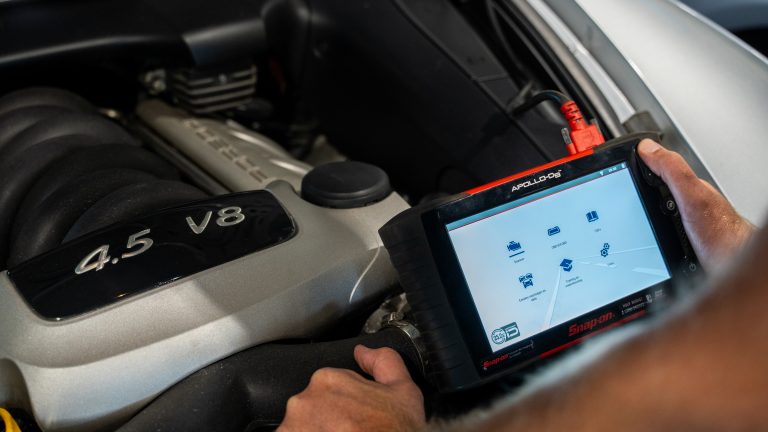 Monteur houdt een Snap-on APOLLO-D8 diagnosetablet vast boven de open motorkap van een auto met een 4.5 V8-motor.