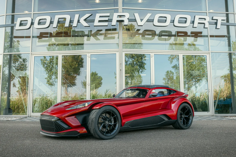 Een felrode Donkervoort‑sportwagen geparkeerd voor een modern glazen gebouw met de naam DONKERVOORT boven de ingang.