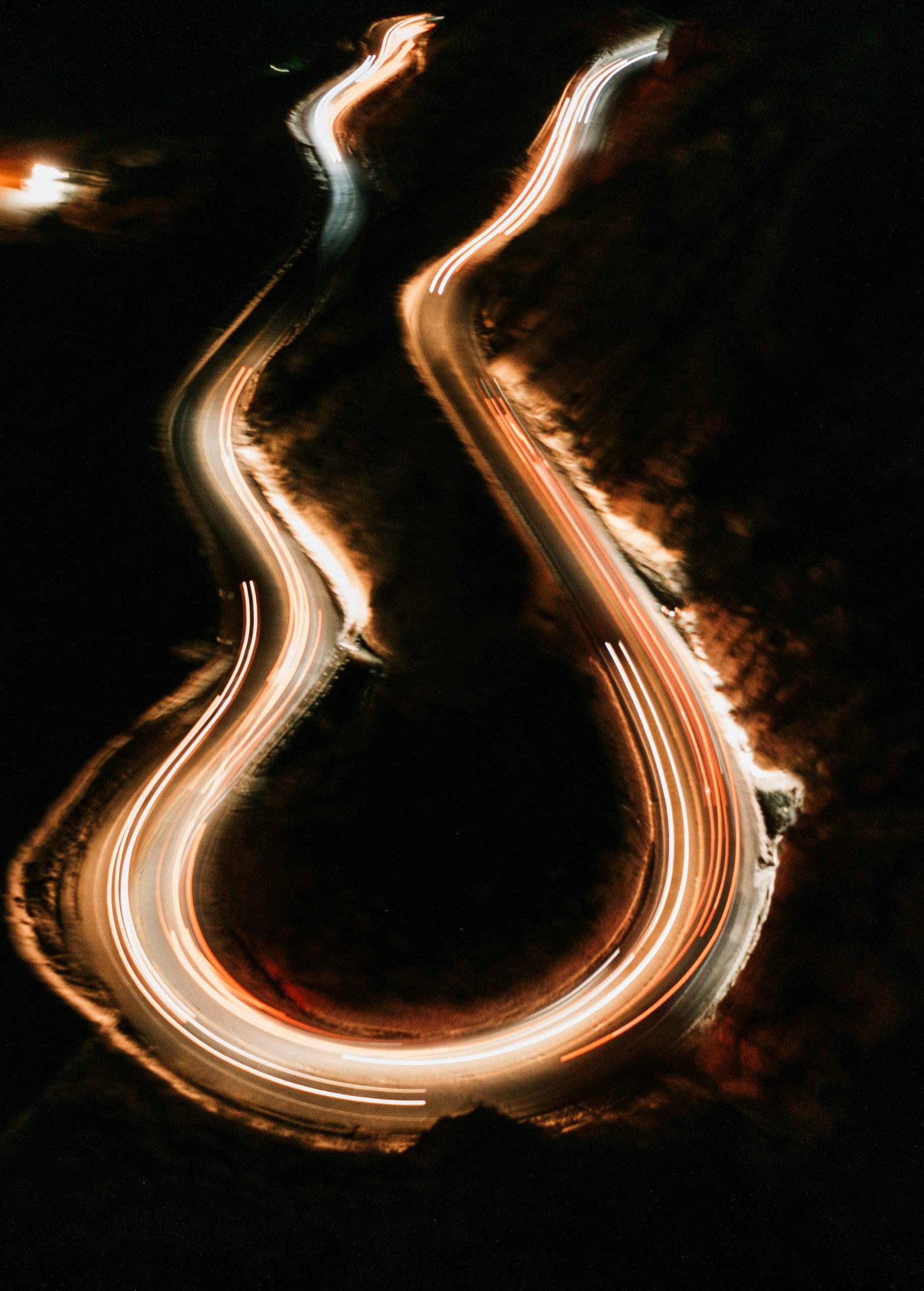 Een bochtige bergweg ’s nachts met felgekleurde lichtsporen van passerende voertuigen.