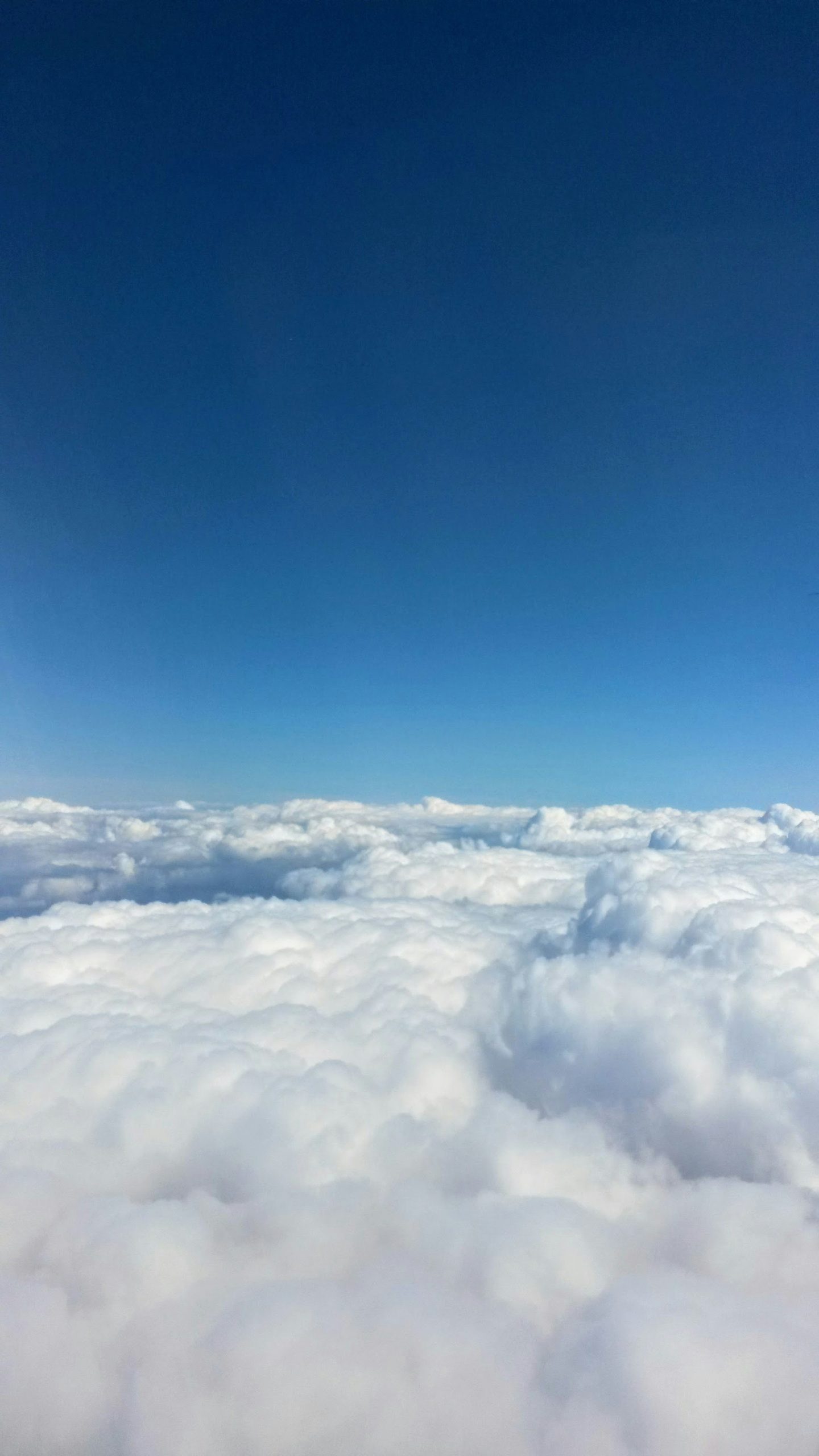 Een uitzicht boven een dikke laag witte wolken met daarboven een helderblauwe lucht.