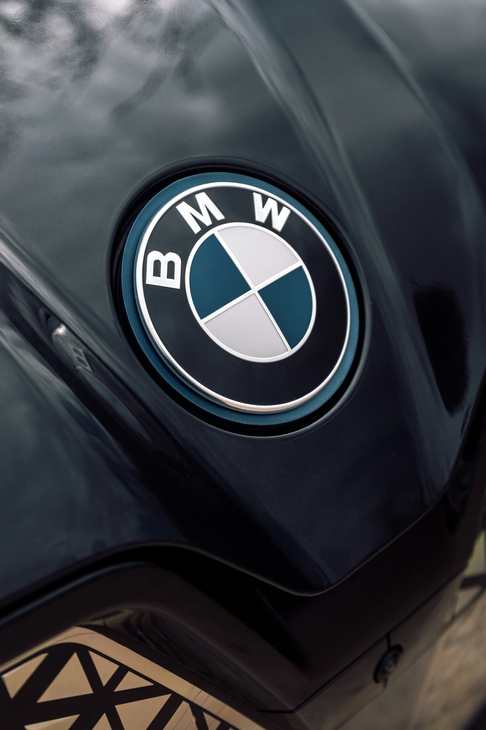 Een close-up van het logo van BMW op een glanzende motorfiets, met reflecties van bomen op de lak.