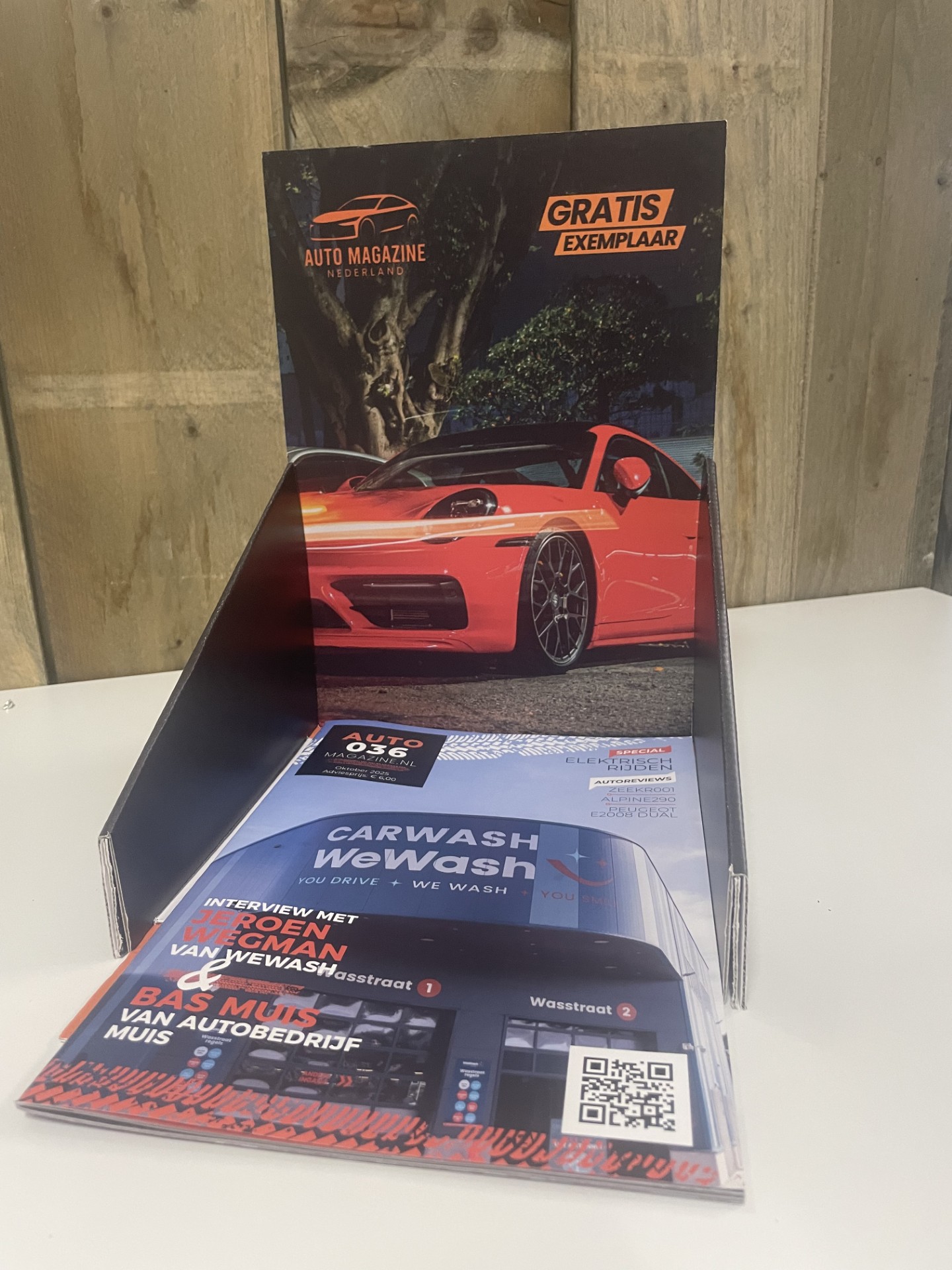Display met gratis auto magazine in een houder, met op de cover een rode sportauto en op de voorgrond een tijdschrift over carwash en auto-interviews.