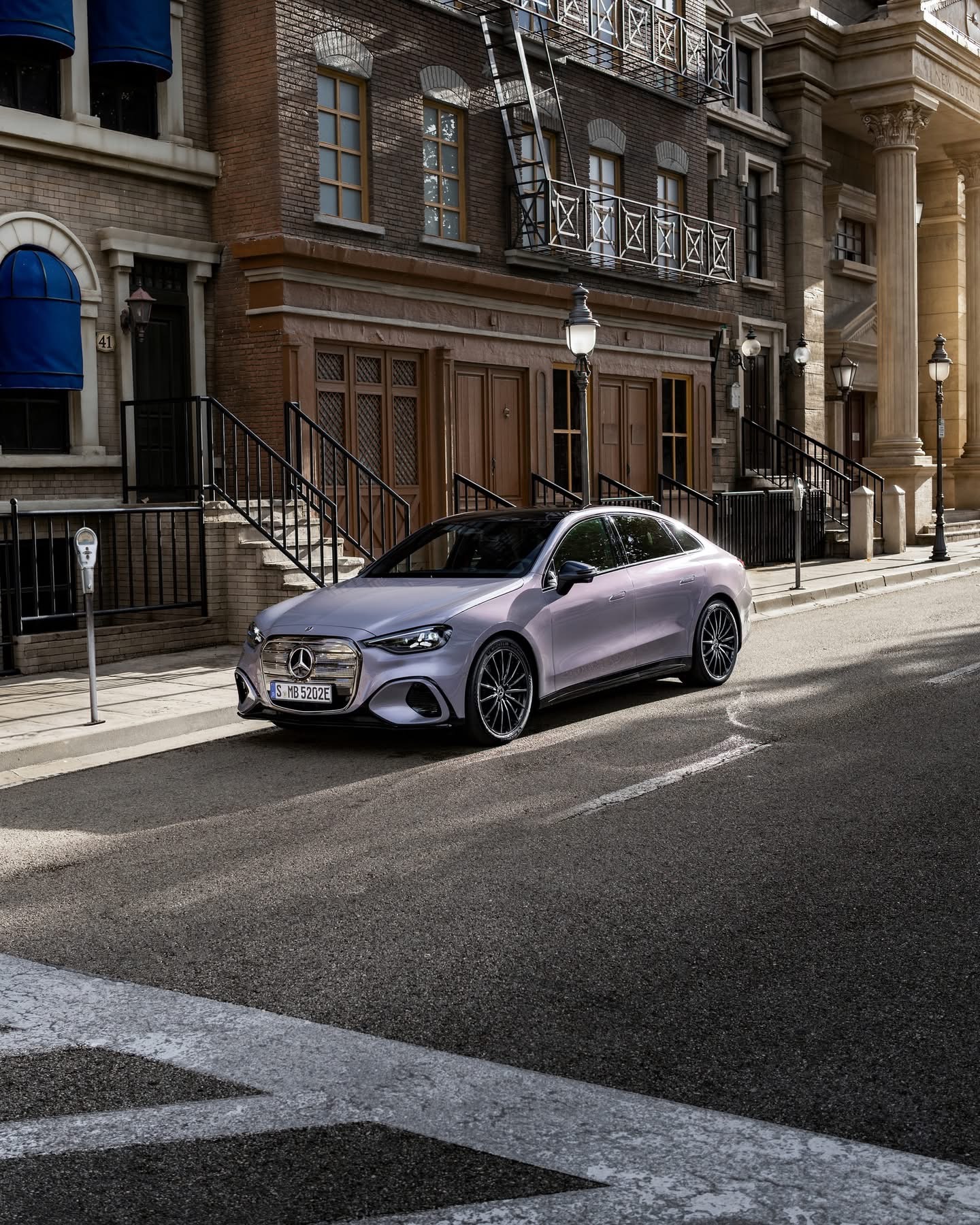 Zilveren Mercedes‑Benz sedan geparkeerd in een klassieke stadsstraat met bakstenen gevels en metalen trapleuningen.