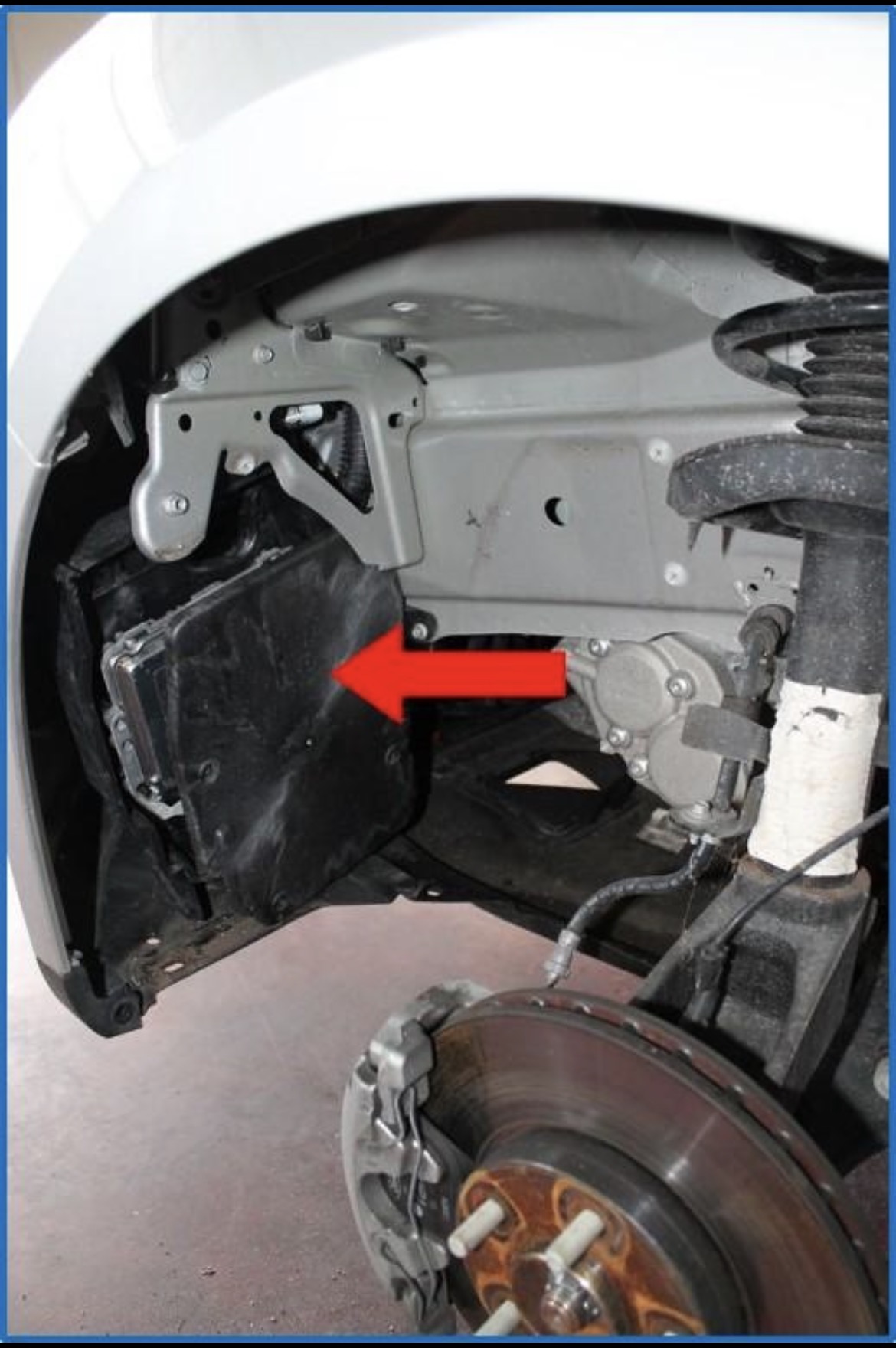 Open wielkast met zichtbaar veersysteem, remschijf en een elektronisch component achter de bekleding, aangeduid met een rode pijl.