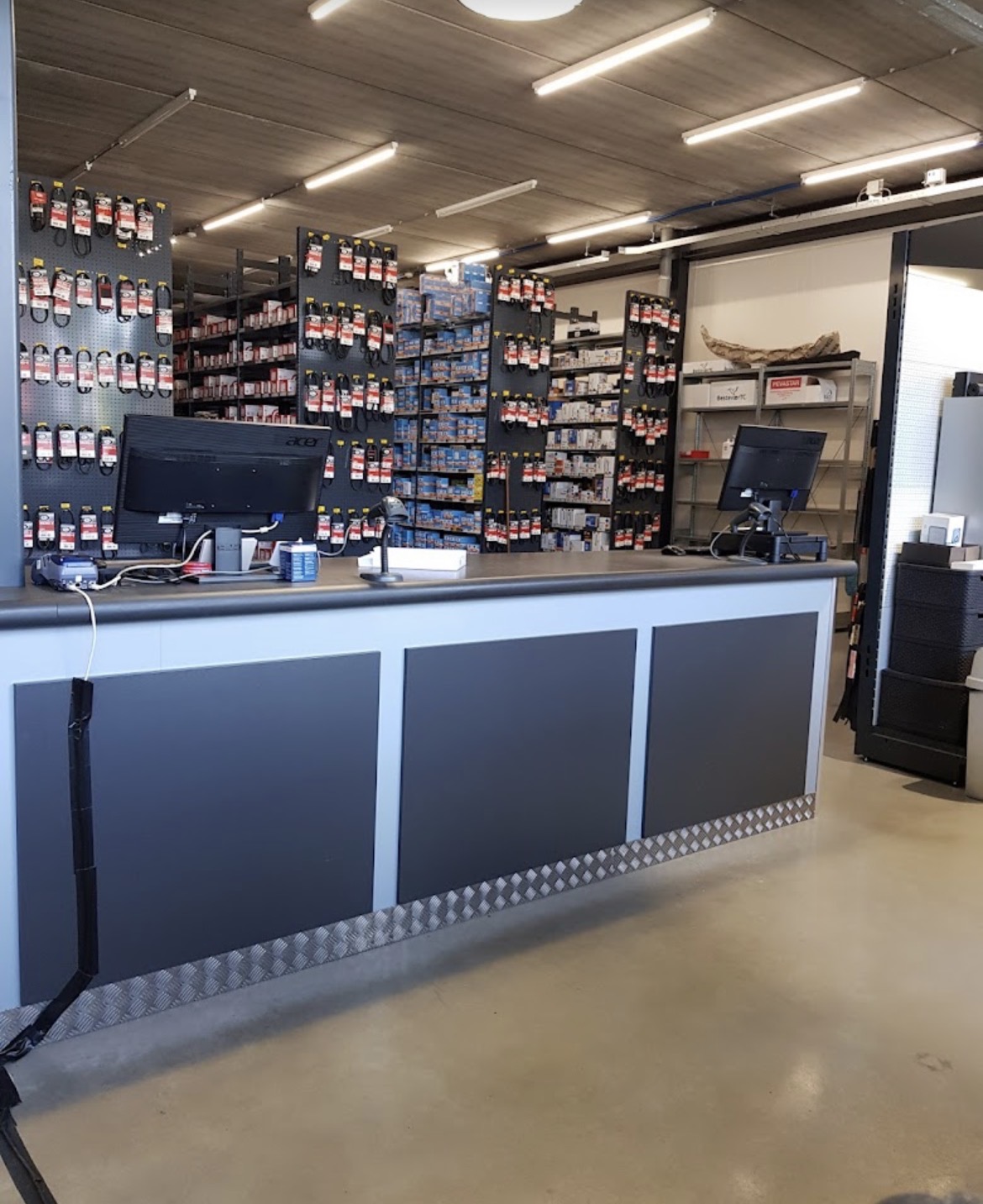 Balie met computers in een automaterialenzaak, met daarachter schappen vol onderdelen en accessoires.