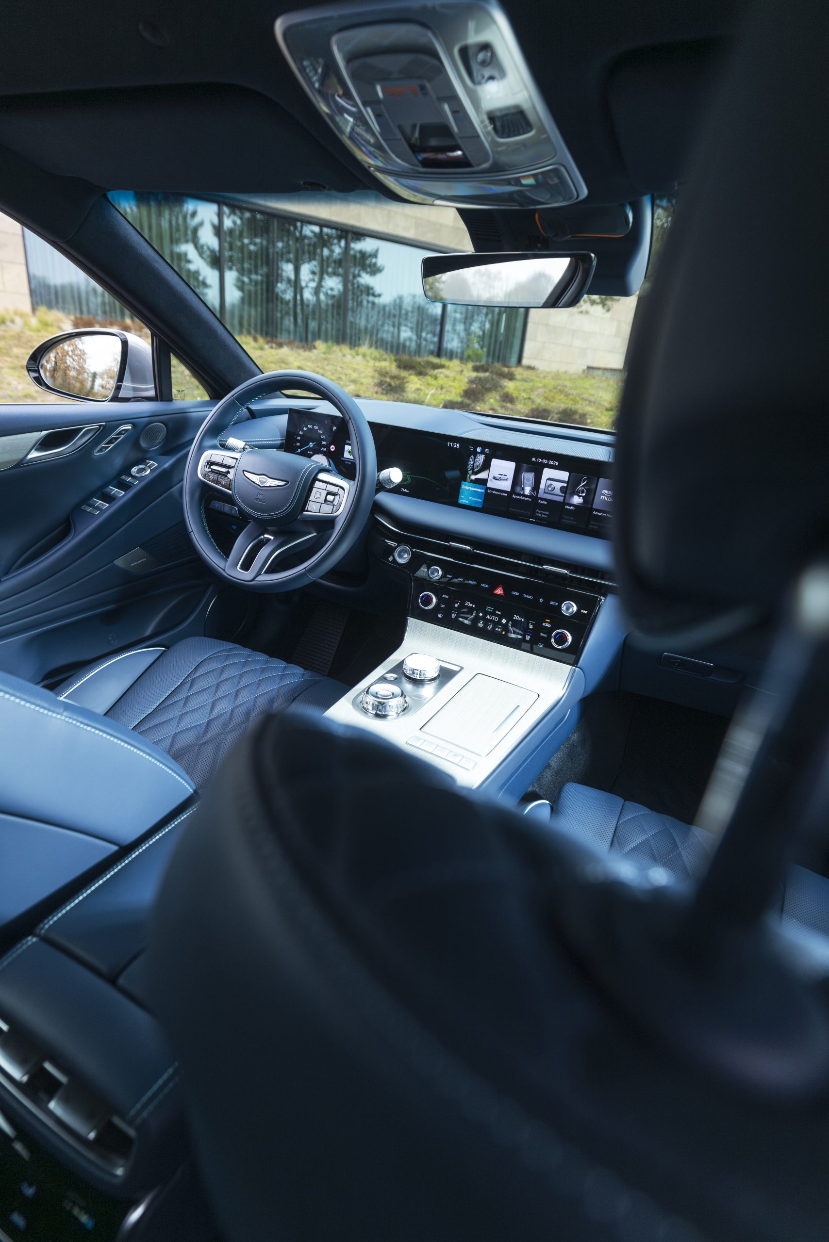 Modern interieur van de Genesis G80 Electrified met digitaal dashboard, groot infotainmentscherm en luxe lederen afwerking, gezien vanaf de achterbank.