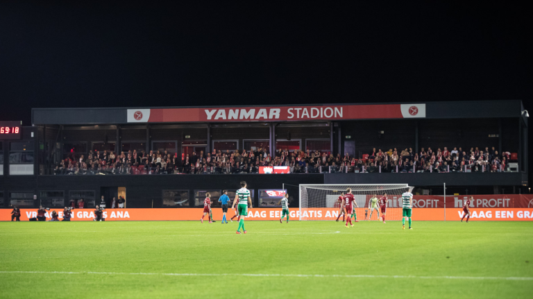 Avondwedstrijd in het Yanmar Stadion met spelers op het veld, volle tribunes en verlichte reclameborden langs de zijlijn.