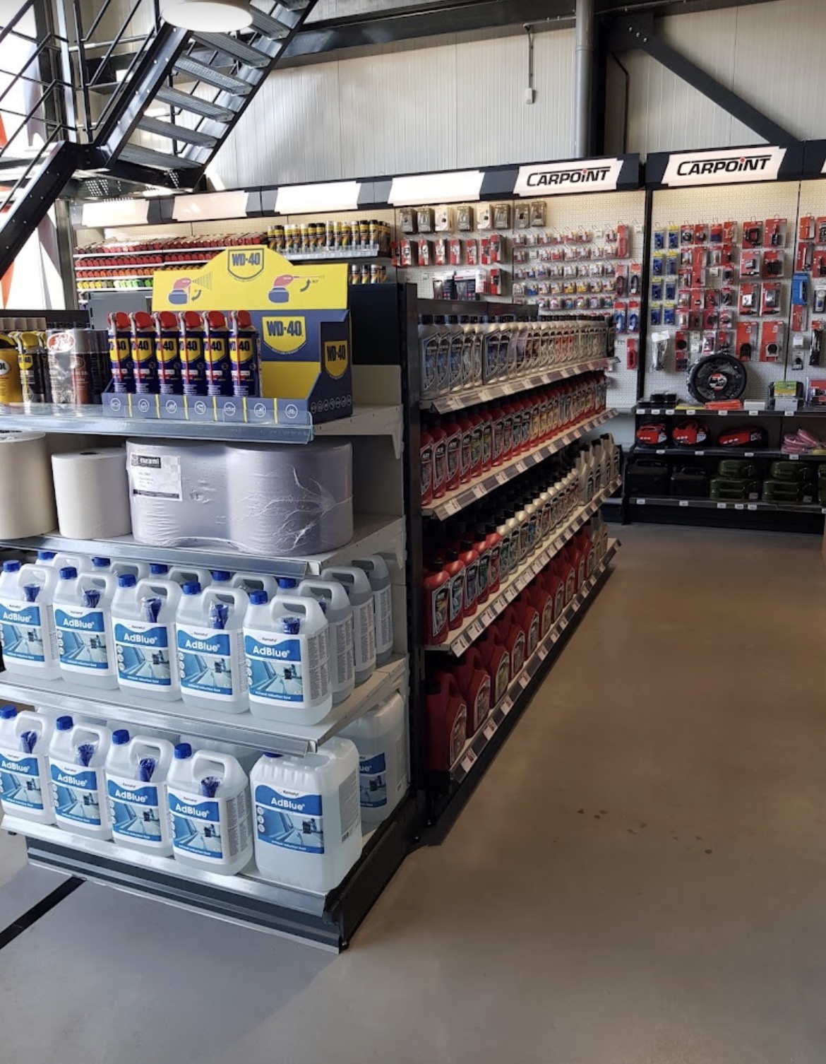 Rekken vol automaterialen zoals AdBlue, WD‑40 en motorolie in een overzichtelijke winkel met metalen schappen.