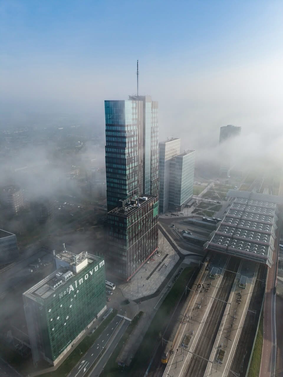 Luchtfoto van een moderne stad met glazen torens, lichte mist en een groot station met glazen dak.