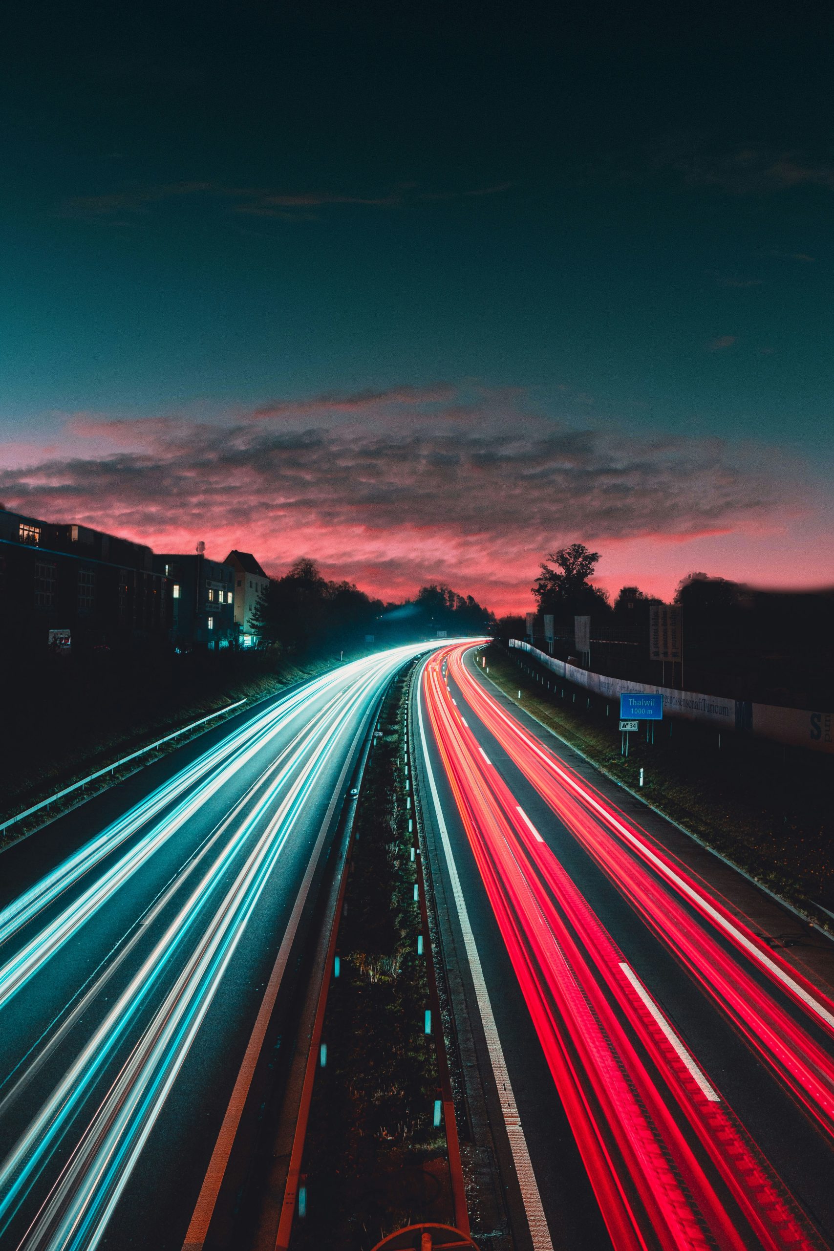 Long‑exposure foto van een snelweg met lichtstrepen van auto's onder een kleurrijke avondlucht.