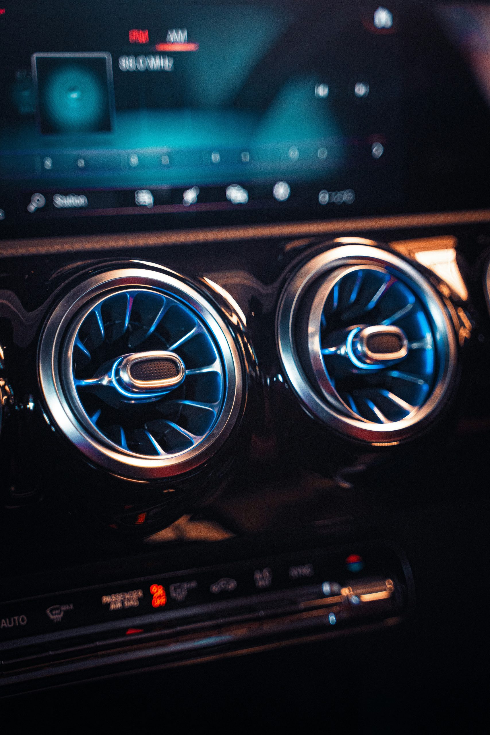 Dashboard van een moderne auto met turbine‑vormige ventilatieroosters met blauwe verlichting en een radioscherm.