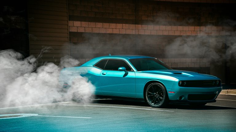 Turquoise Dodge Challenger die een burnout maakt, met rook rond de achterwielen tegen een bakstenen muur.