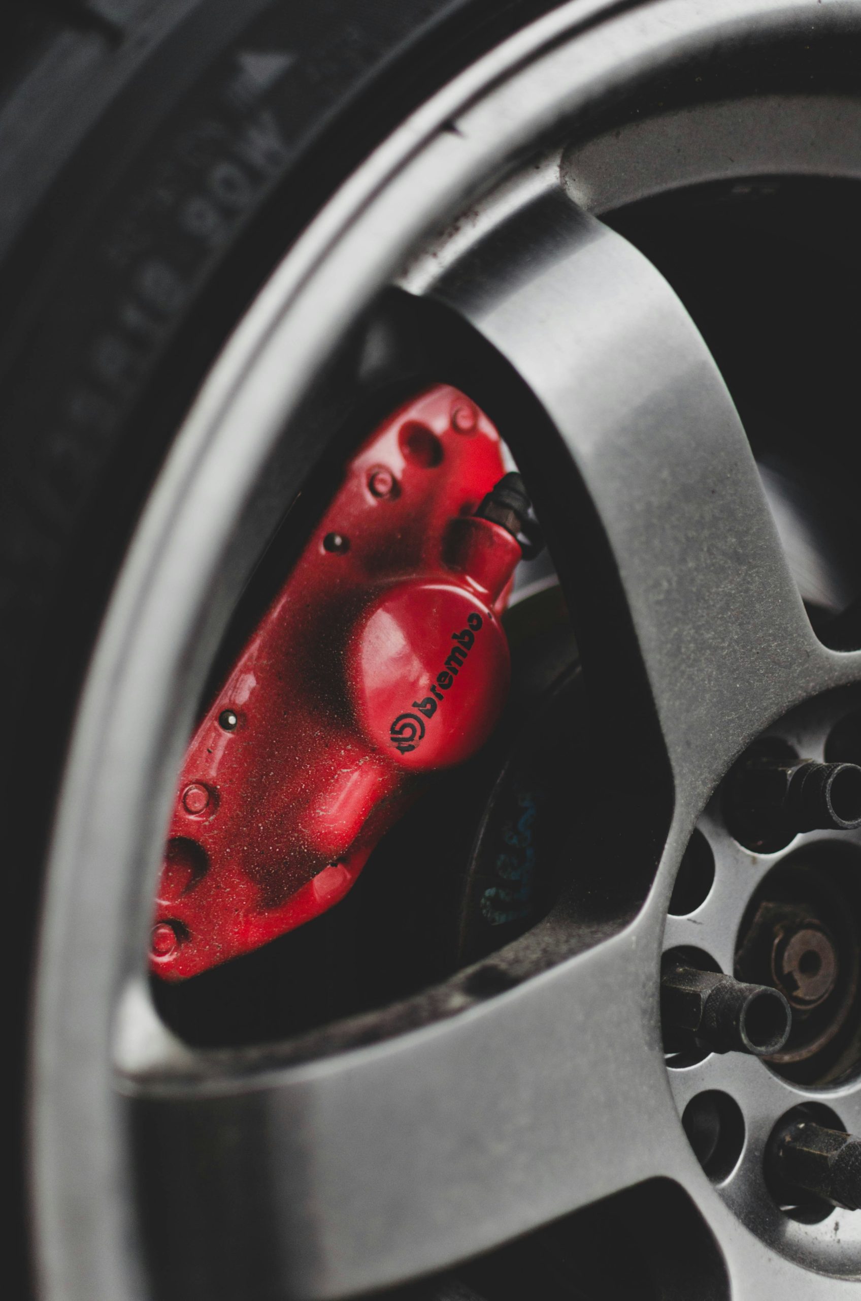 Close‑up van een metallic velg met rode Brembo‑remklauw en zichtbare wielbouten.