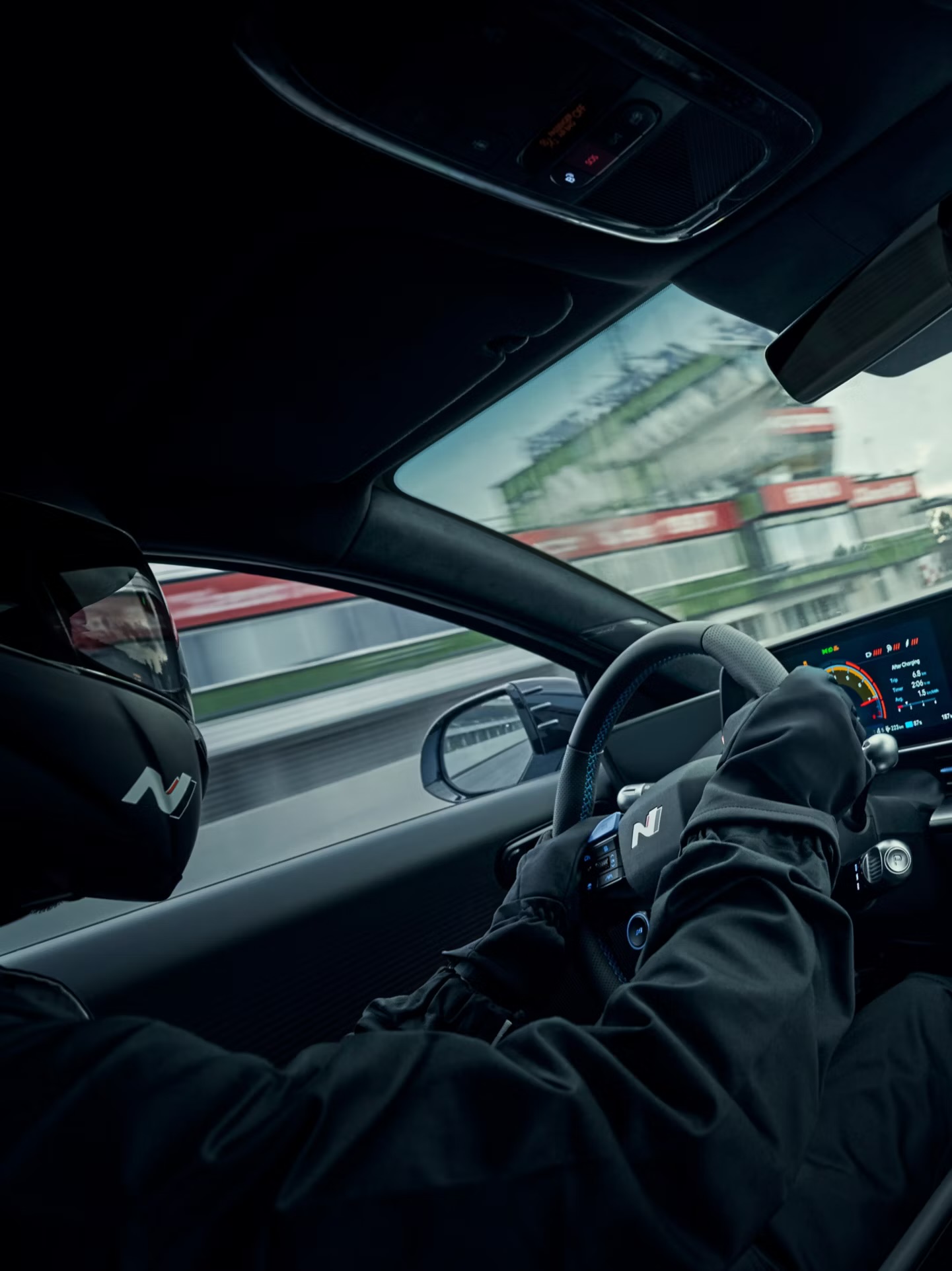 Bestuurder met zwarte N‑helm en handschoenen in een sportieve Hyundai, met digitaal dashboard en circuit op de achtergrond.