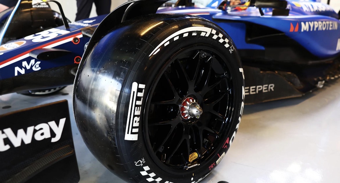 Voorwiel van een Formule‑1‑auto met Pirelli‑slickband, zwarte velg en blauwe body met diverse sponsorlogo’s.