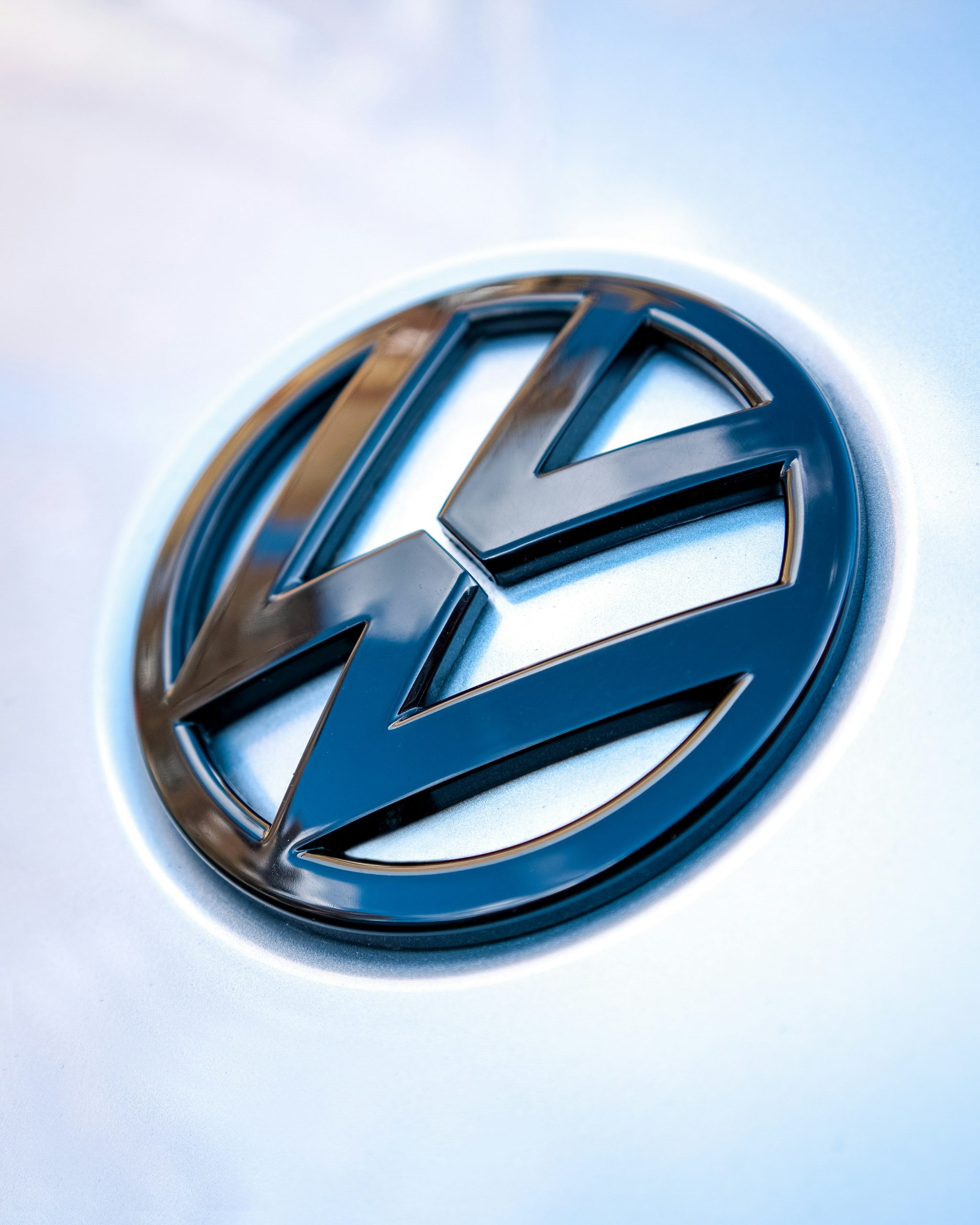 Metallic Volkswagen‑embleem op een lichtgekleurde carrosserie, strak en centraal in beeld.