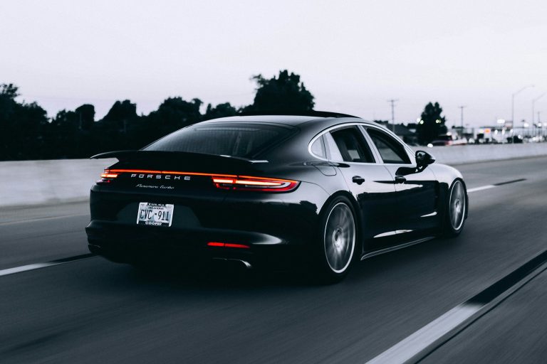 Zwarte Porsche Panamera Turbo rijdend op de snelweg met brandende achterlichten onder een grijze lucht.