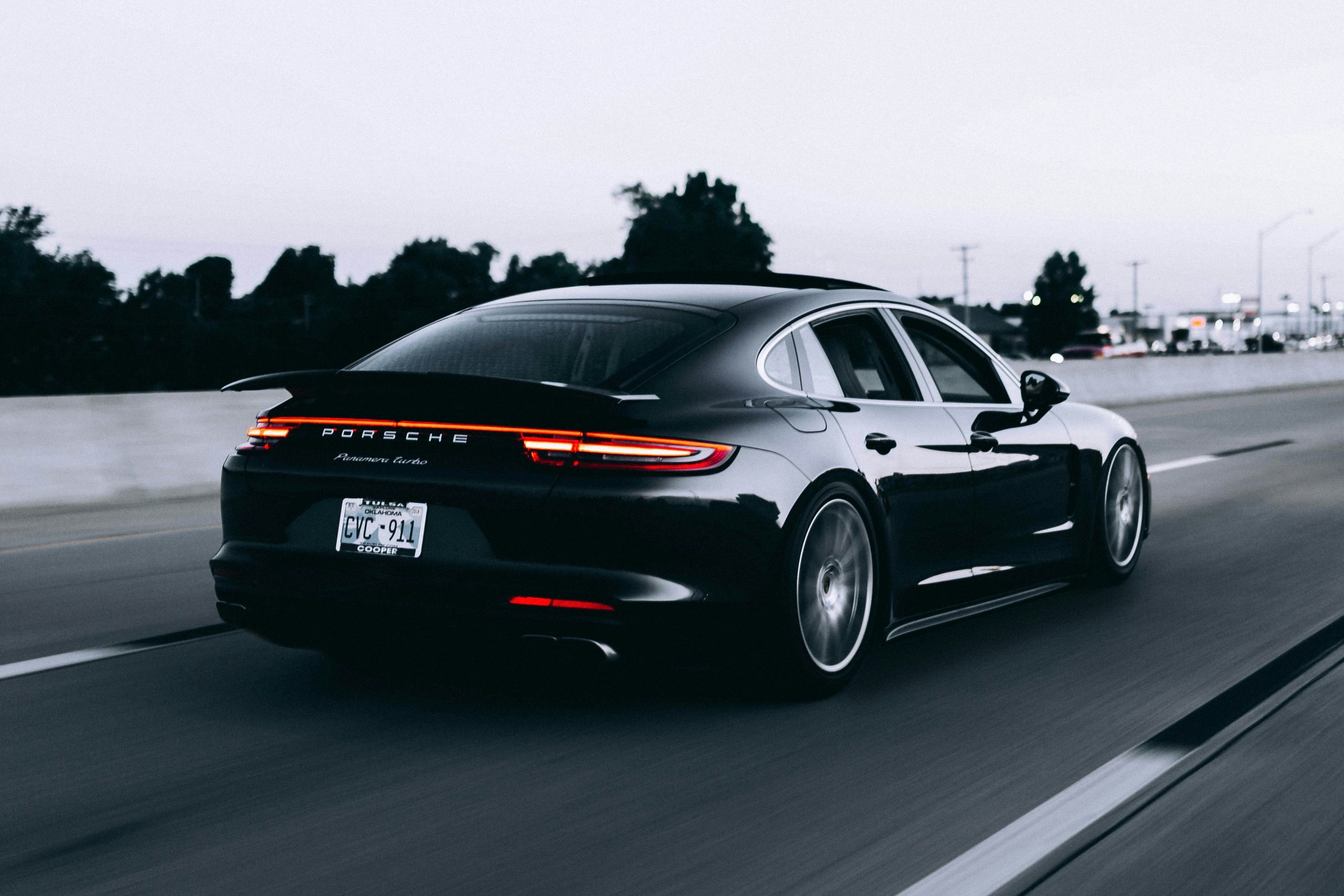 Zwarte Porsche Panamera Turbo rijdend op de snelweg met brandende achterlichten onder een grijze lucht.