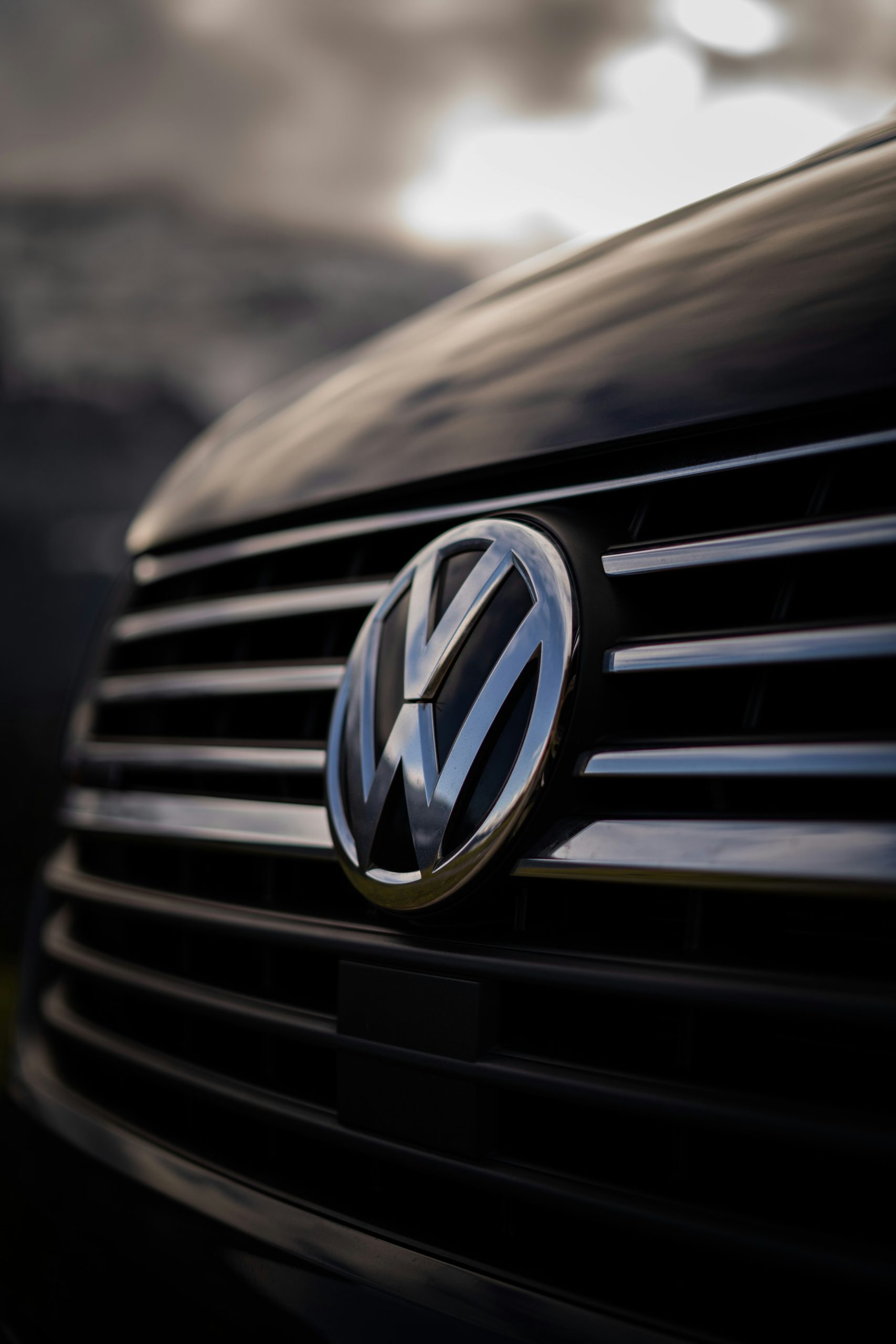 Close‑up van het chromen Volkswagen‑logo op een metallic grille met horizontale lijnen en zachte reflecties.