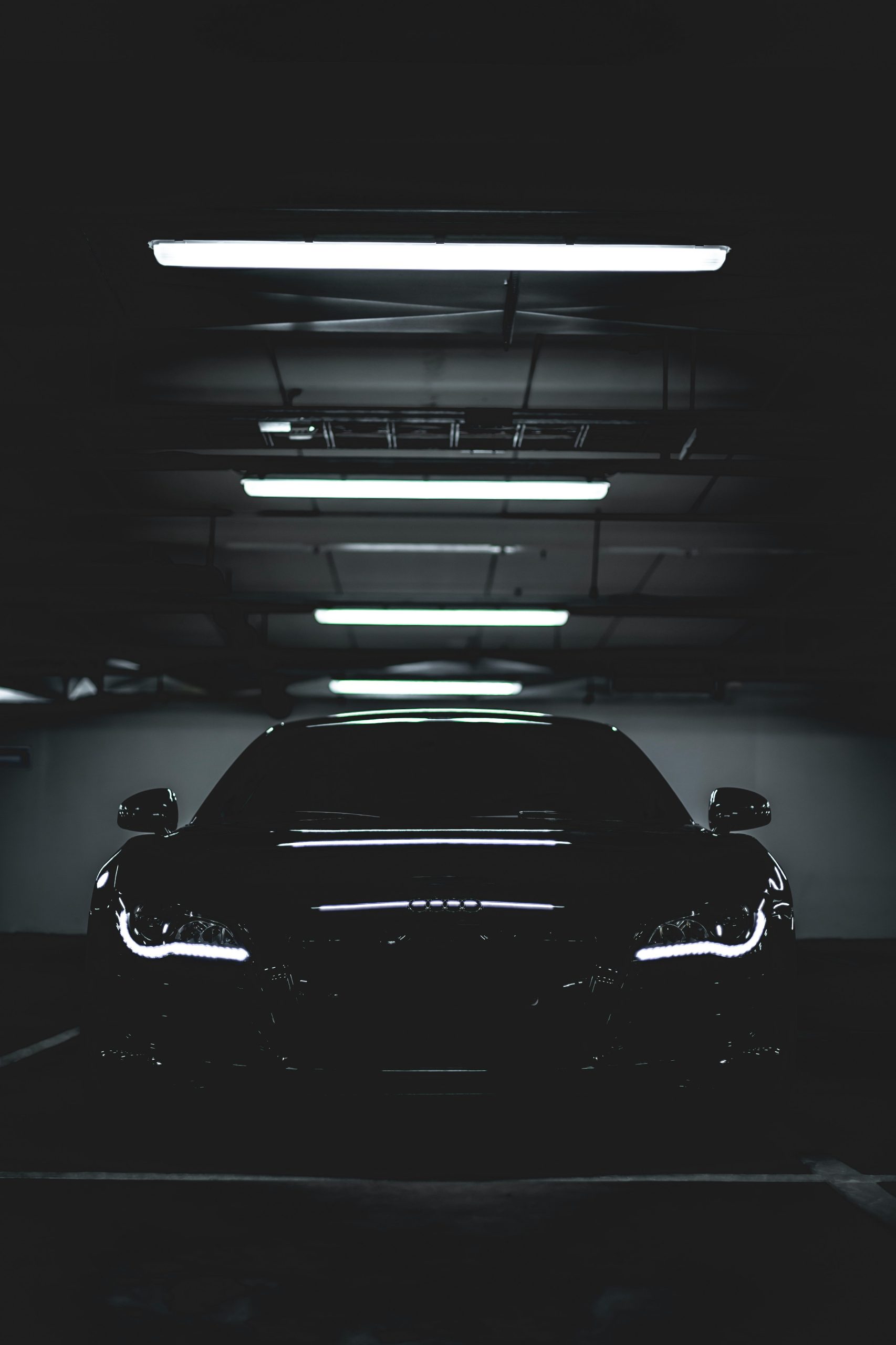 Zwarte Audi‑sportwagen geparkeerd in een donkere parkeergarage met felle koplampen en reflecties op de lak.