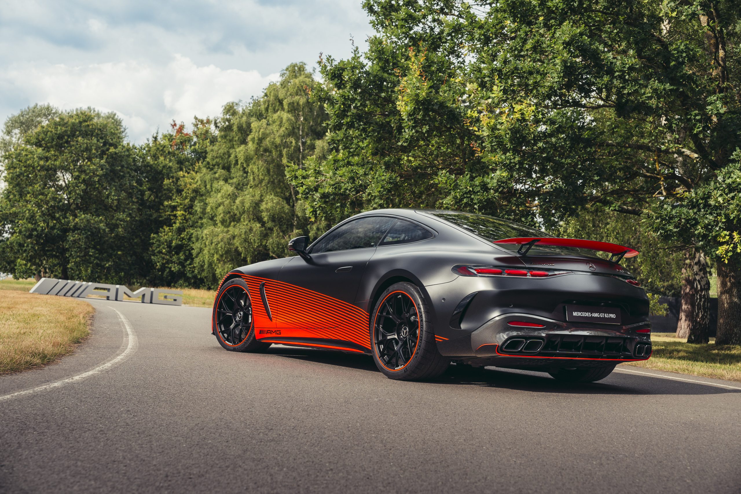 Een matte zwarte Mercedes-AMG GT Black Series met oranje details staat op een bochtige weg met bomen op de achtergrond.