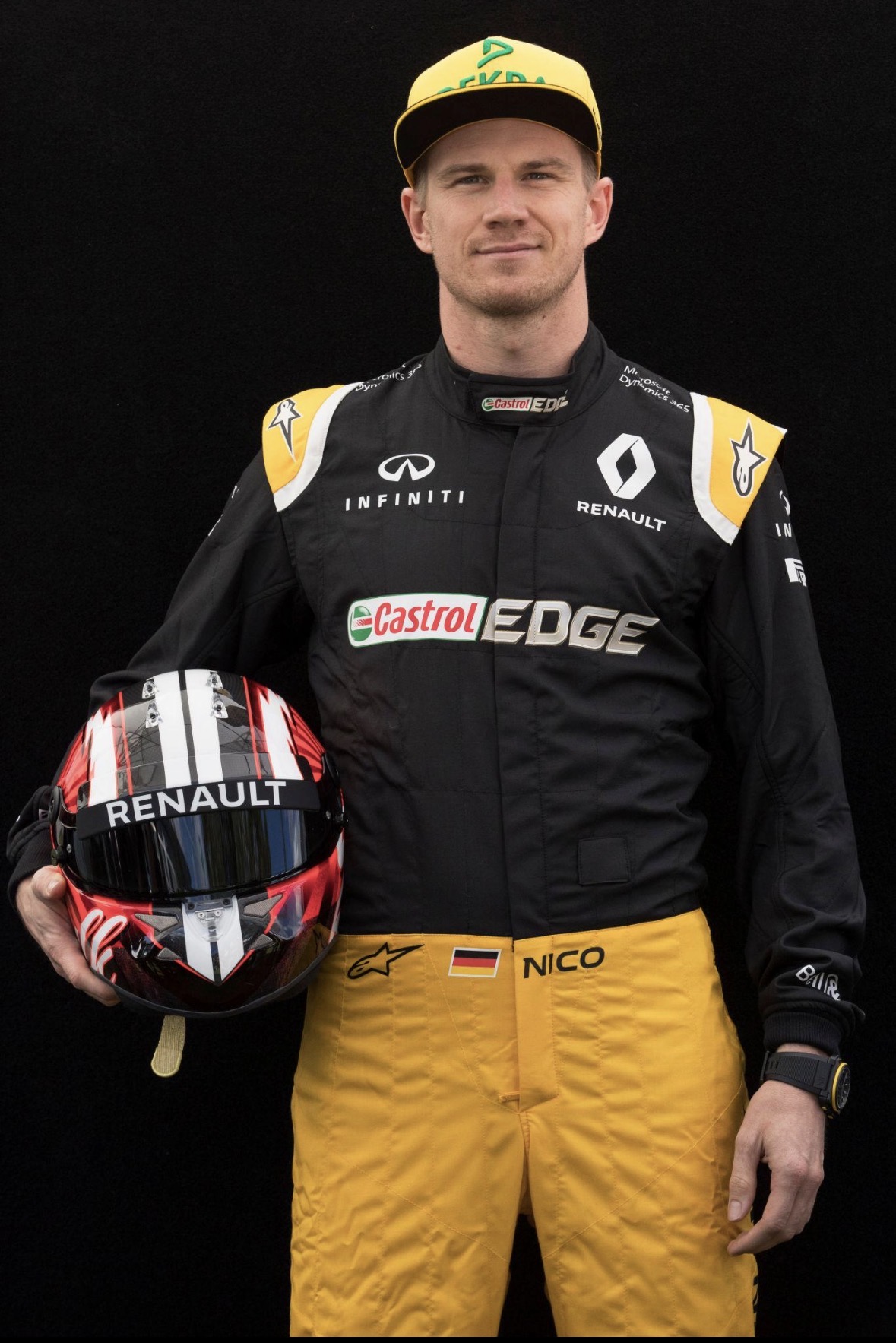 Nico Hülkenberg in zijn Renault-pak met gele broek, een pet op en zijn racehelm in zijn hand.