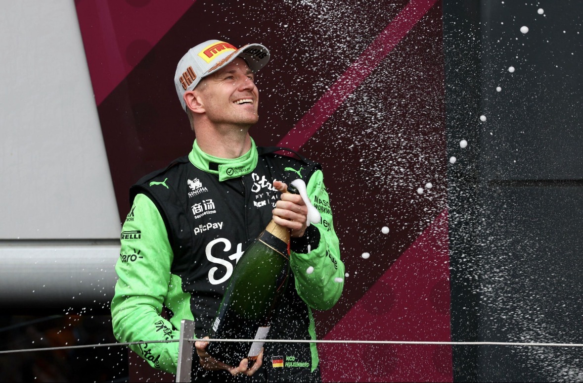 Nico Hülkenberg viert op het podium terwijl hij champagne spuit, gekleed in een groen en zwart racepak.