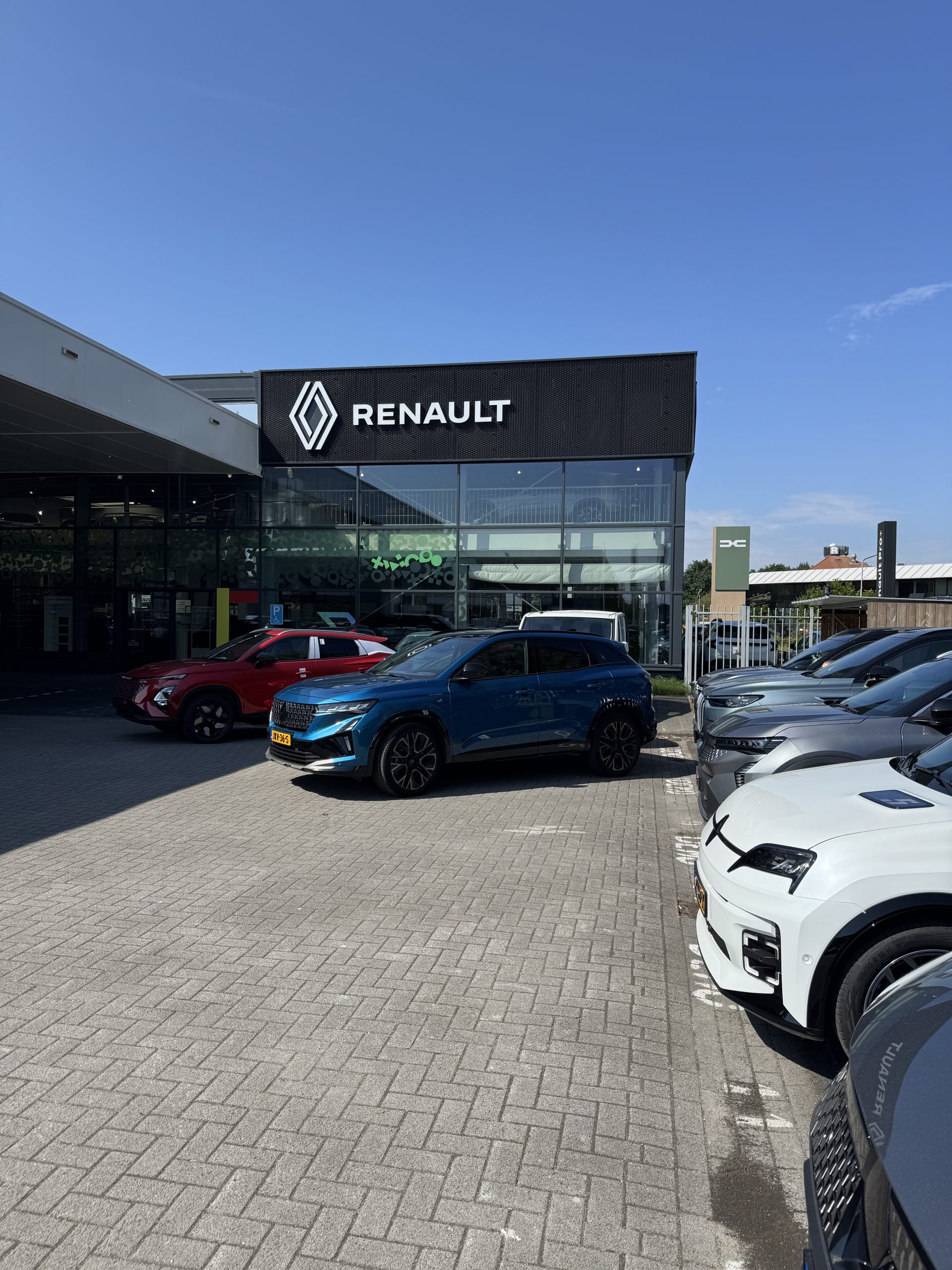 Moderne Renault showroom met zwarte gevel, grote glazen ramen en meerdere geparkeerde auto’s voor de ingang.