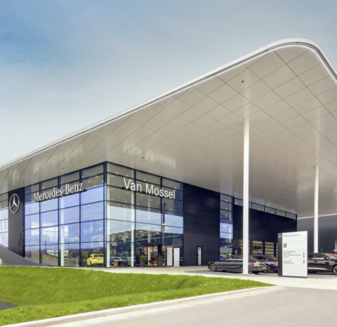 Moderne Mercedes‑Benz Van Mossel showroom met glazen gevel, luxe uitstraling en meerdere auto’s voor de ingang.