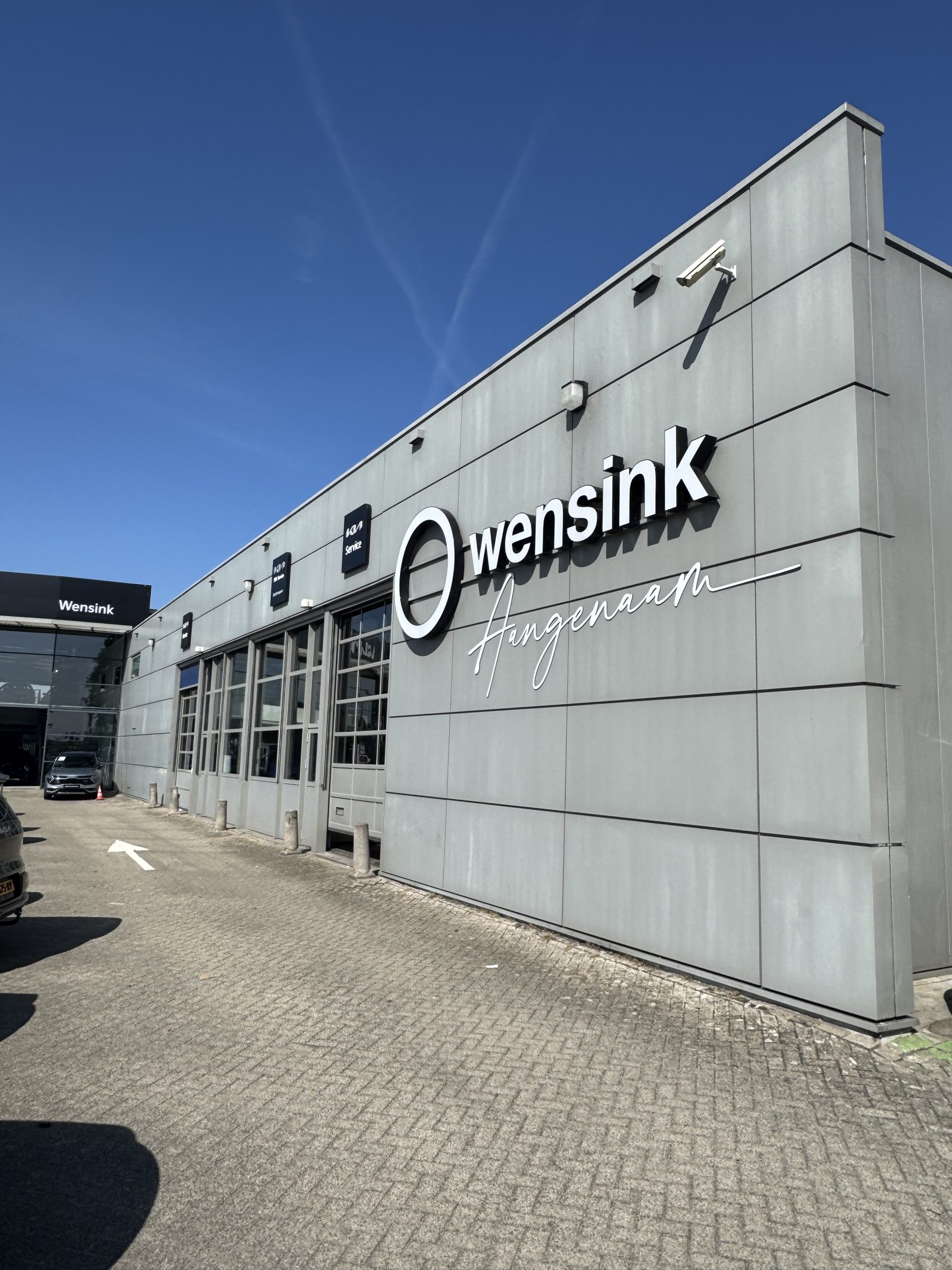 Voorkant van het moderne Wensink Angenaam-dealershipgebouw met grote logo en strakke gevel.