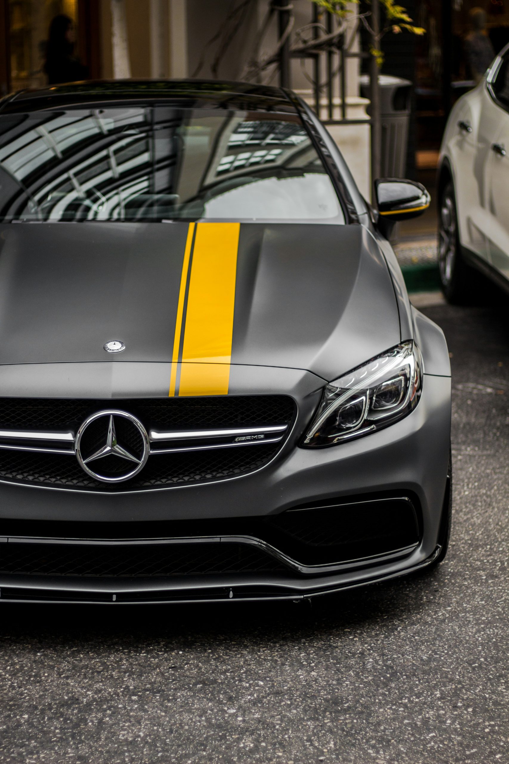 Matgrijze Mercedes‑AMG met opvallende gele striping op de motorkap en agressieve sportieve voorzijde.