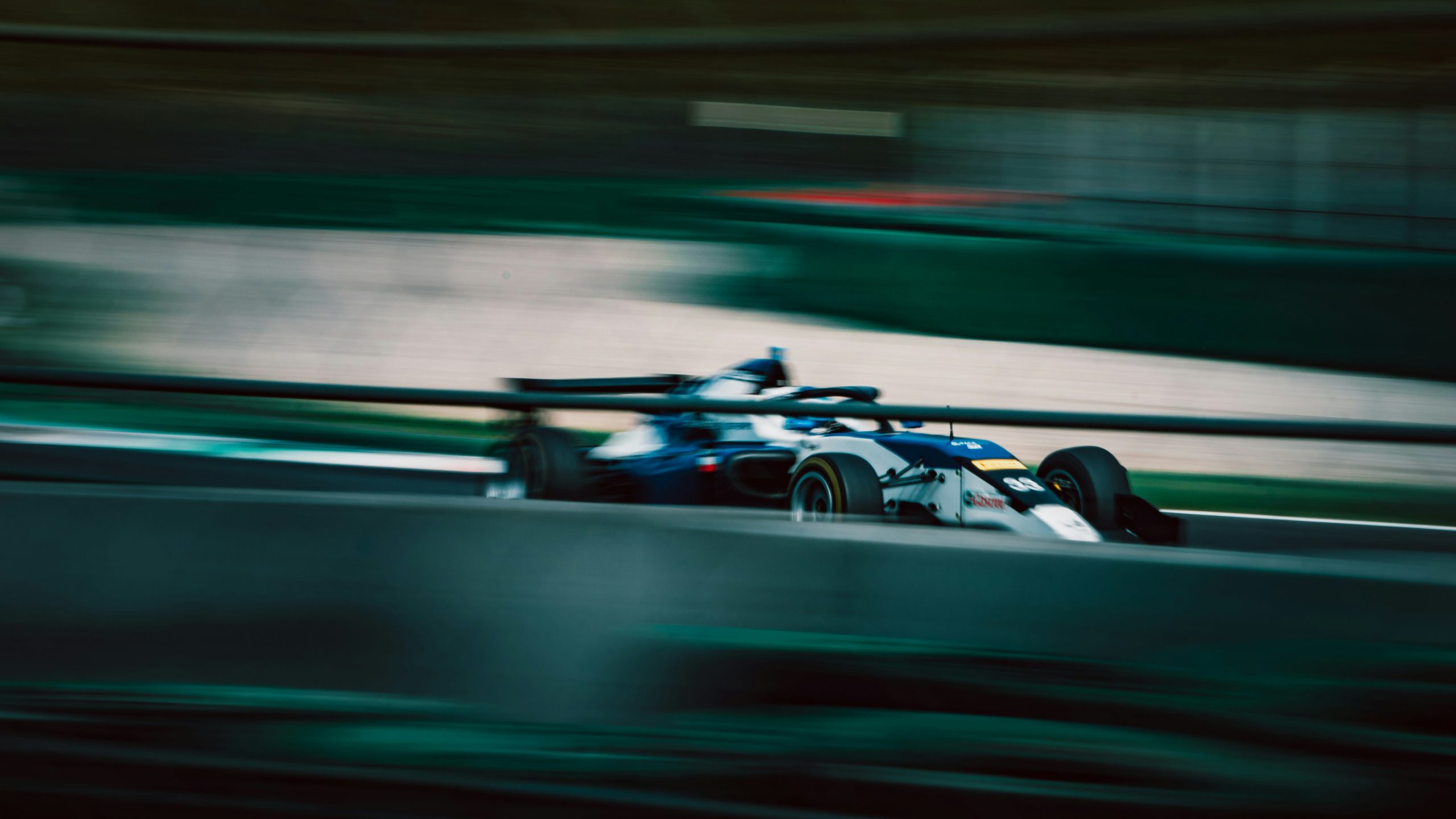 Wit‑blauwe formulewagen met startnummer 99 rijdend op hoge snelheid, vastgelegd met sterke motion blur.