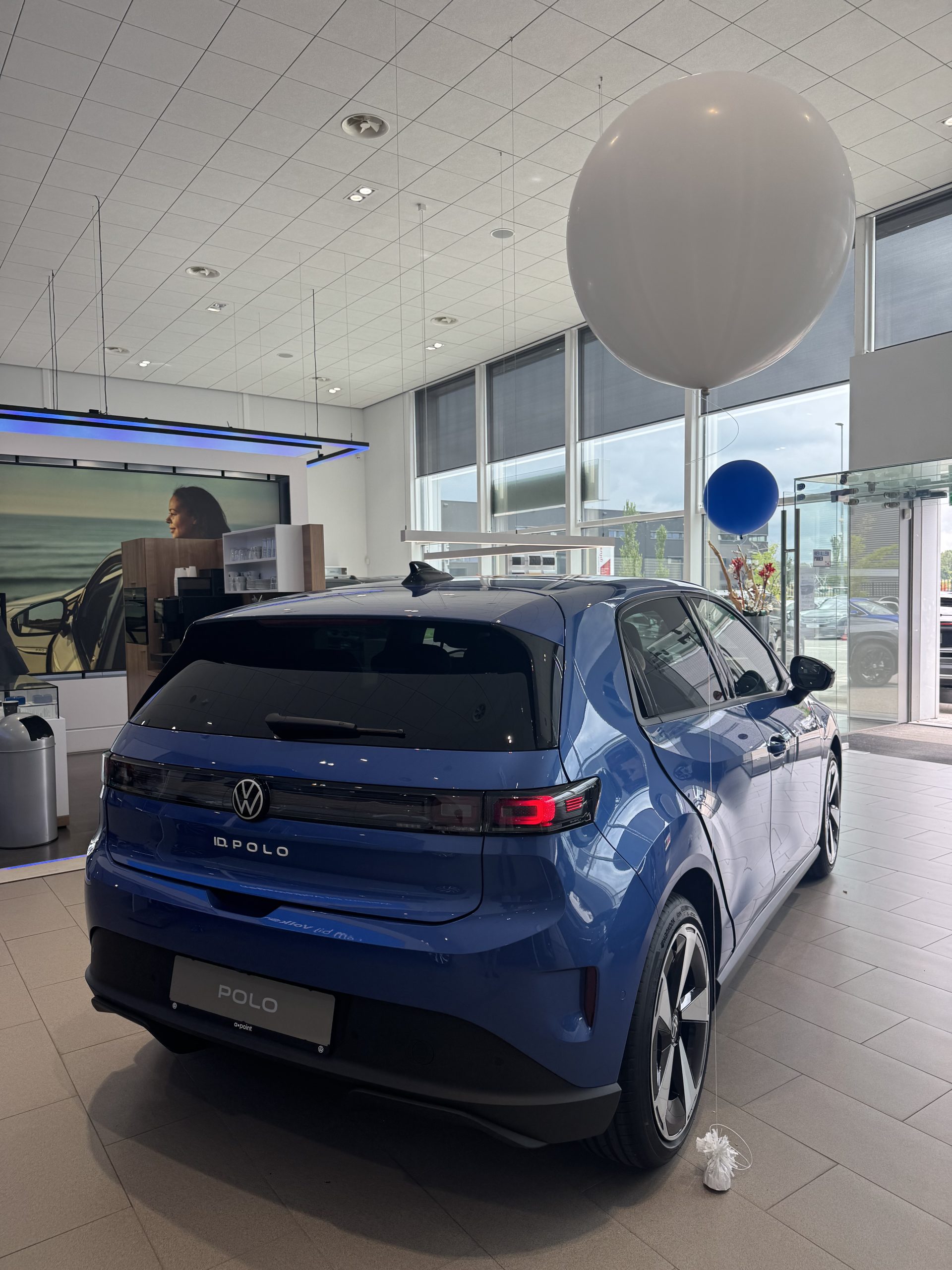 Blauwe elektrische Volkswagen met aerodynamisch design en grote velgen in lichte showroom met ‘Welkom bij Volkswagen’ bord.