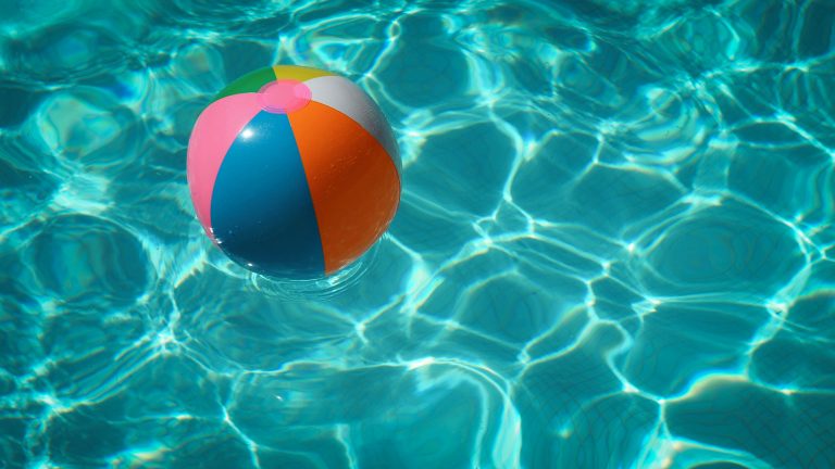 Een kleurrijke strandbal drijft op het heldere, turquoise water van een zwembad.